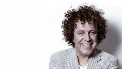 Leo Sayer dressed in a grey blazer, looking straight to camera and smiling
